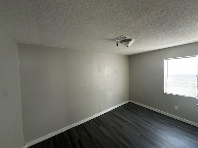 unfurnished room with dark wood-type flooring, a textured ceiling, and baseboards