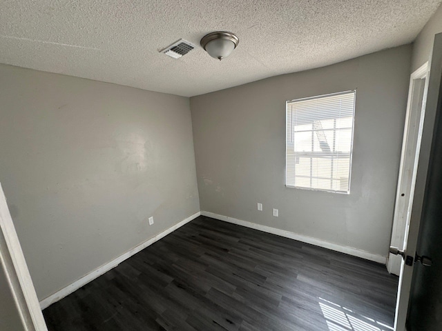 unfurnished bedroom with baseboards, a textured ceiling, visible vents, and dark wood-type flooring