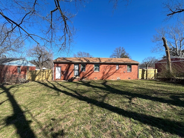 rear view of house featuring crawl space, a yard, fence, and brick siding