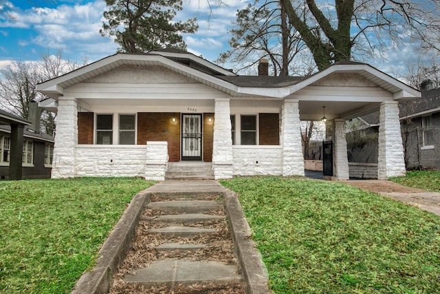 view of front of house with stone siding, a chimney, a porch, and a front yard