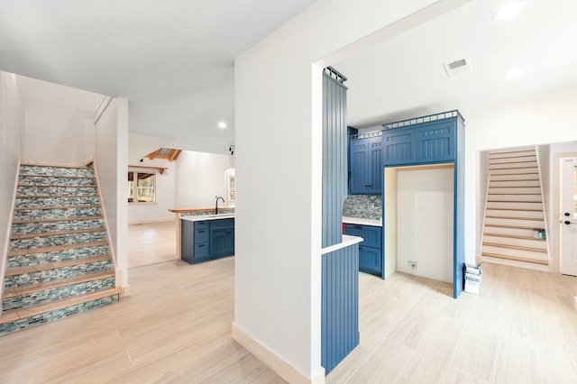 hall with visible vents, light wood-style flooring, stairs, a sink, and recessed lighting