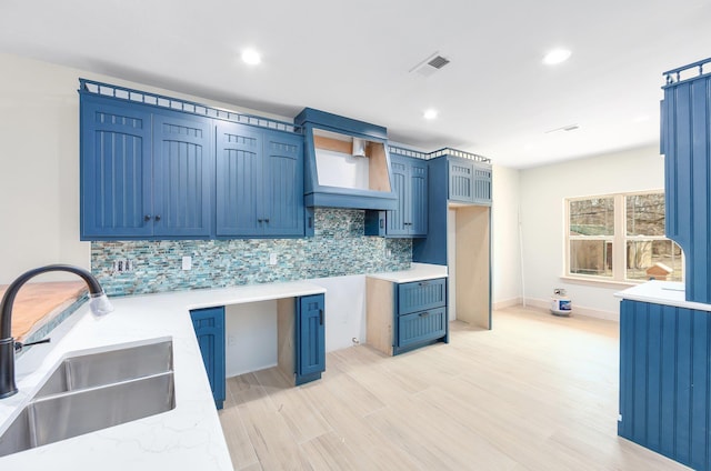 kitchen with visible vents, light wood-style flooring, backsplash, a sink, and light stone countertops