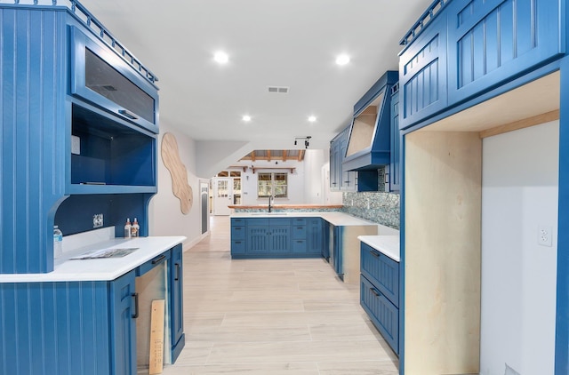 kitchen featuring blue cabinets, tasteful backsplash, glass insert cabinets, and custom range hood