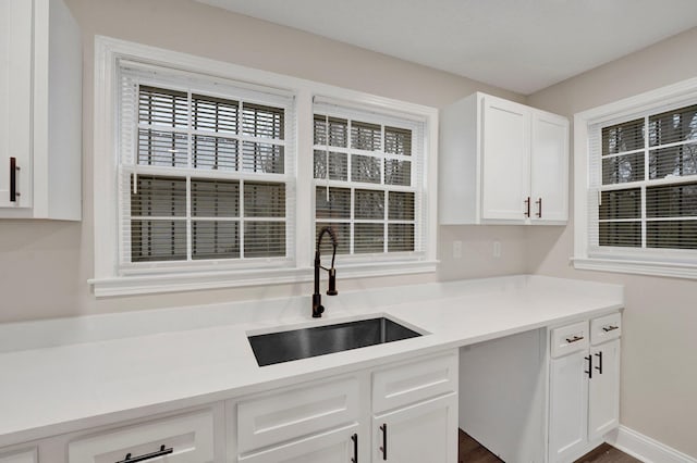 kitchen with white cabinets, baseboards, light countertops, and a sink