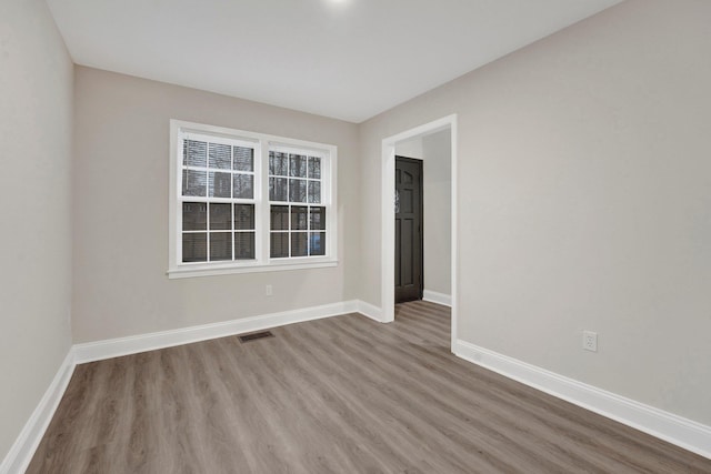 spare room with baseboards, visible vents, and wood finished floors