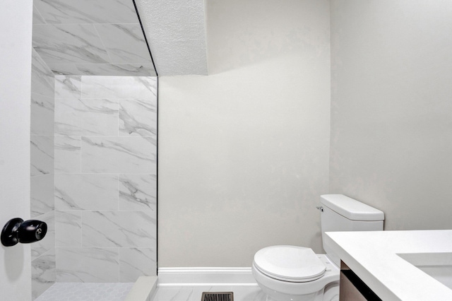 full bath featuring visible vents, toilet, vanity, tiled shower, and baseboards