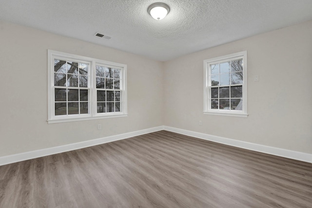 unfurnished room with a textured ceiling, wood finished floors, visible vents, and baseboards