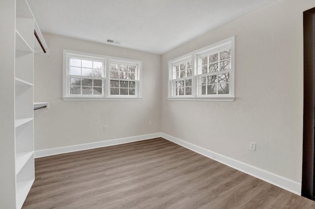 spare room featuring visible vents, plenty of natural light, baseboards, and wood finished floors