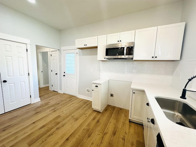 kitchen featuring decorative backsplash, stainless steel microwave, light wood-type flooring, white cabinetry, and a sink