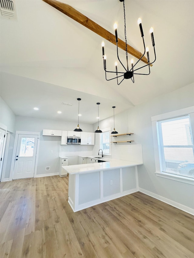 kitchen featuring lofted ceiling with beams, a peninsula, a sink, light wood-type flooring, and stainless steel microwave