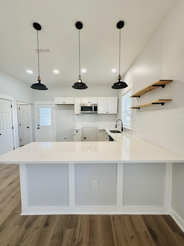 kitchen featuring visible vents, stainless steel microwave, wood finished floors, a peninsula, and a sink