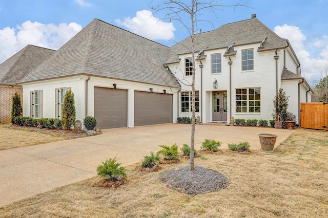 french provincial home with roof with shingles, driveway, and an attached garage