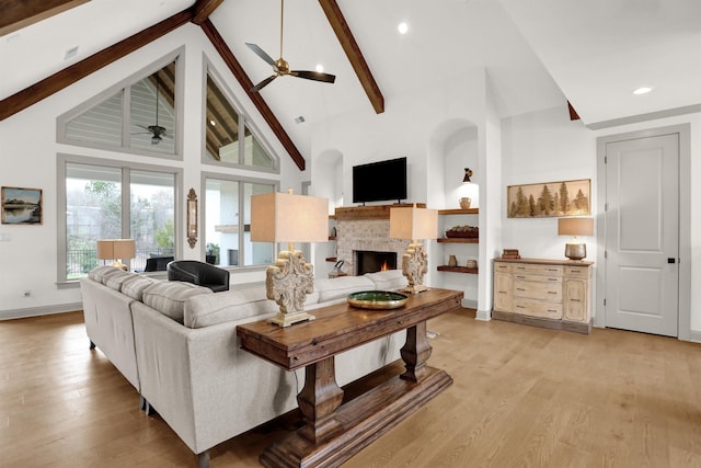 living room featuring high vaulted ceiling, a fireplace, baseboards, light wood-style floors, and beam ceiling