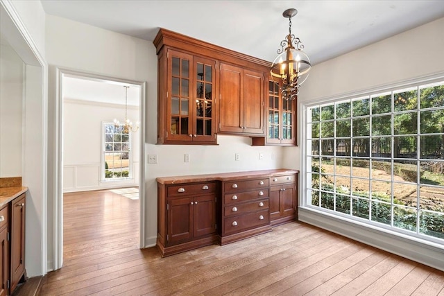 kitchen with light wood-style flooring, glass insert cabinets, light countertops, a chandelier, and pendant lighting