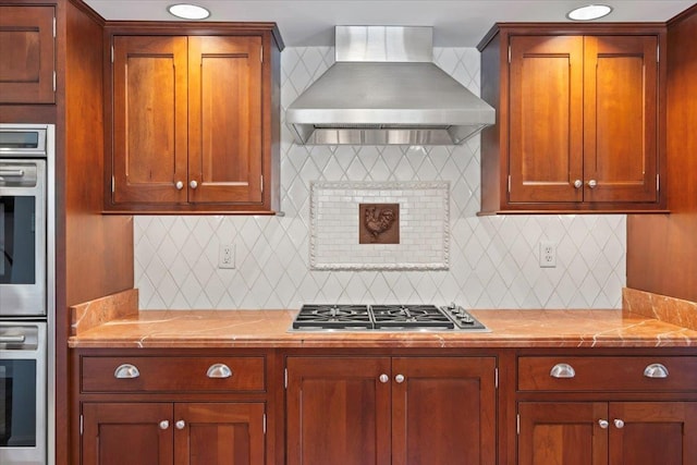 kitchen featuring stainless steel gas cooktop, wall chimney exhaust hood, backsplash, and light countertops