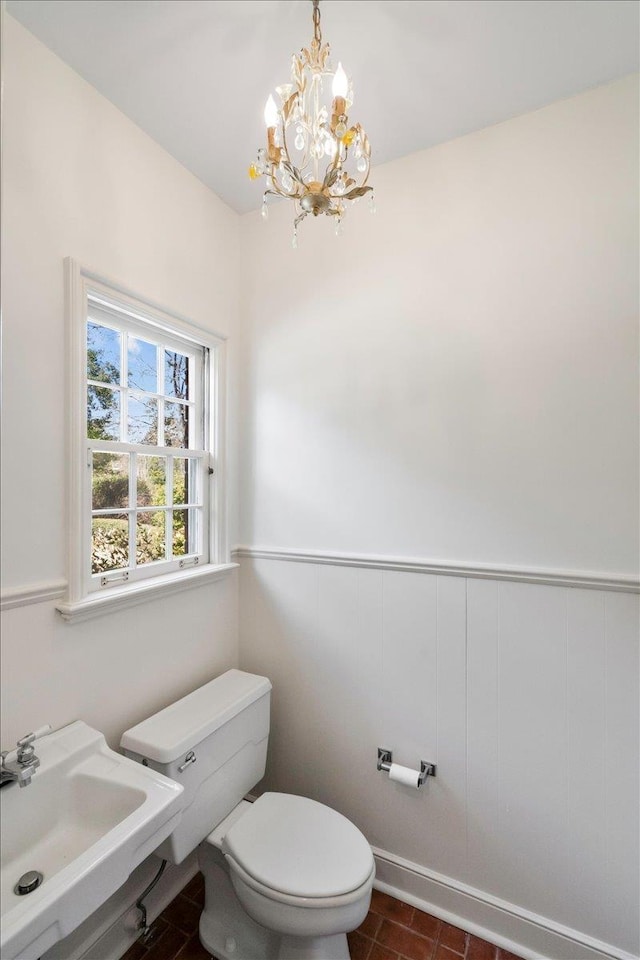 half bath with toilet, an inviting chandelier, a sink, and wainscoting