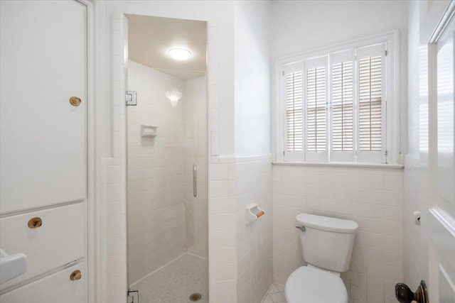 full bath with toilet, a stall shower, tile walls, and wainscoting