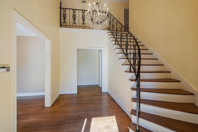 staircase with a notable chandelier, a high ceiling, baseboards, and wood finished floors