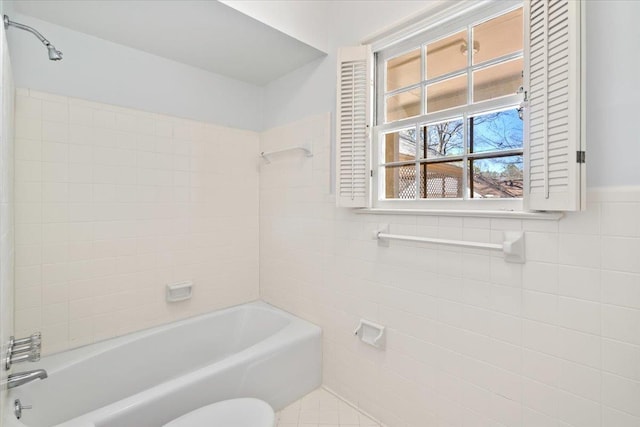 bathroom with washtub / shower combination, wainscoting, tile walls, and toilet