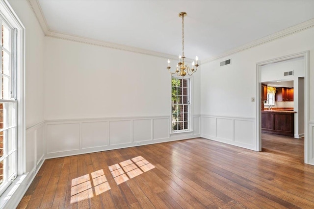 empty room with ornamental molding, hardwood / wood-style flooring, visible vents, and an inviting chandelier