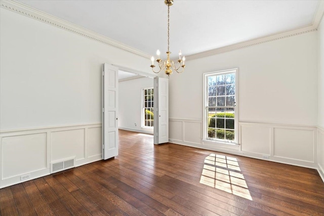 unfurnished dining area featuring visible vents, wainscoting, dark wood-style floors, ornamental molding, and an inviting chandelier