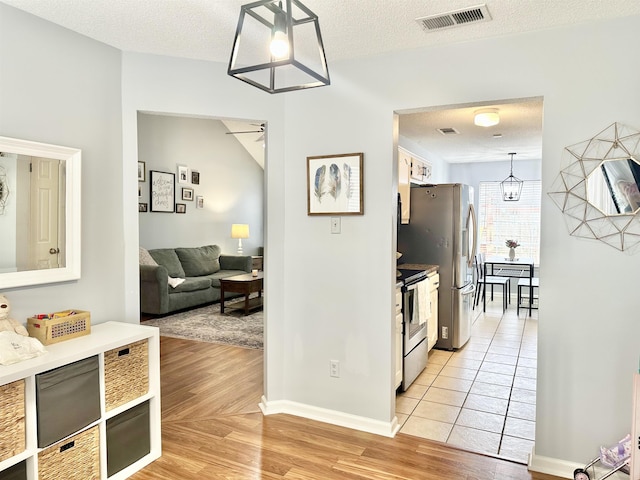 hallway with light wood-type flooring, visible vents, a chandelier, and a textured ceiling