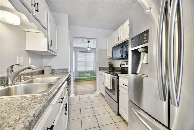 kitchen with light tile patterned floors, appliances with stainless steel finishes, white cabinetry, a sink, and a textured ceiling