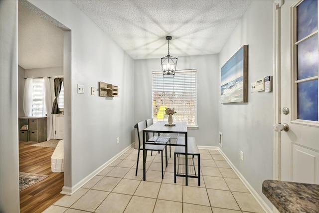 dining space with light tile patterned floors, a textured ceiling, baseboards, and an inviting chandelier