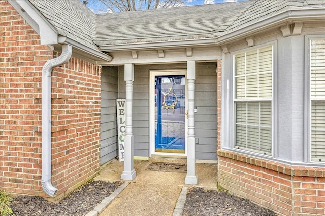 doorway to property featuring brick siding and roof with shingles