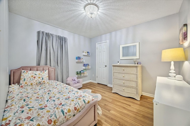 bedroom with a textured ceiling, baseboards, and light wood-style floors