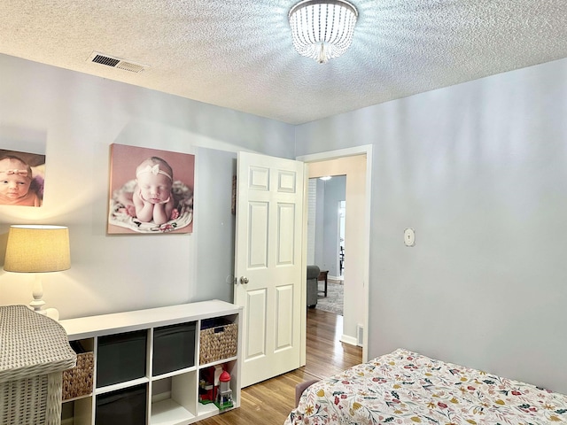 bedroom with a textured ceiling, wood finished floors, and visible vents