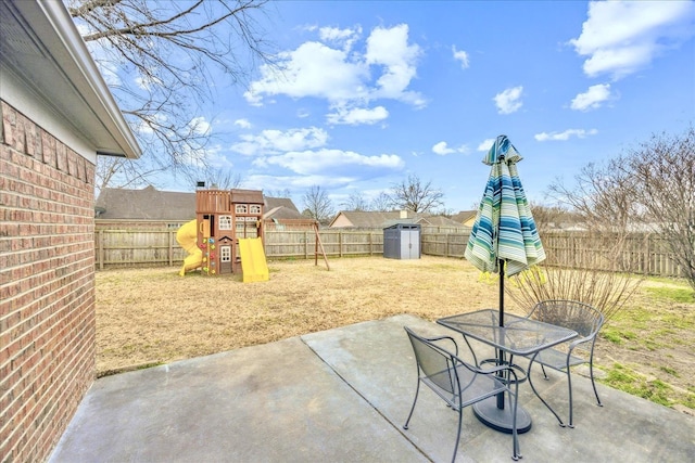 view of patio featuring outdoor dining space, a fenced backyard, a playground, and an outbuilding