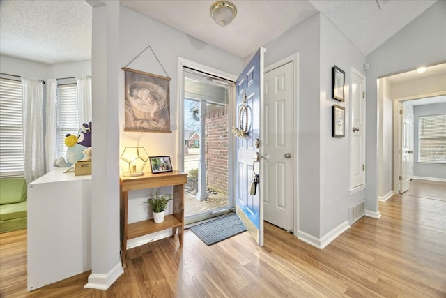 entryway featuring visible vents, baseboards, a textured ceiling, and light wood finished floors