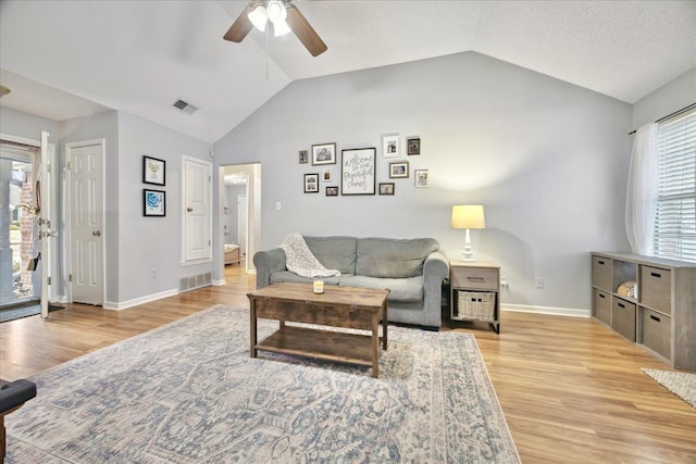 living room featuring light wood-type flooring, baseboards, visible vents, and vaulted ceiling