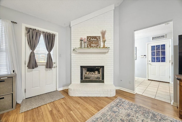 foyer featuring lofted ceiling, a fireplace, a textured ceiling, and wood finished floors