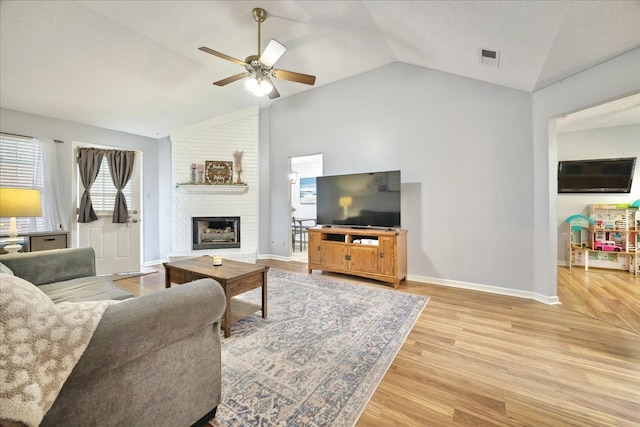 living room with lofted ceiling, a ceiling fan, baseboards, a brick fireplace, and light wood finished floors