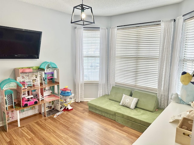 recreation room featuring a textured ceiling, baseboards, and wood finished floors