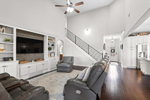 living room featuring baseboards, dark wood finished floors, arched walkways, ceiling fan, and stairway