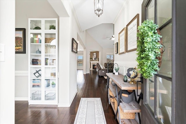 hall with lofted ceiling, baseboards, ornamental molding, and dark wood finished floors