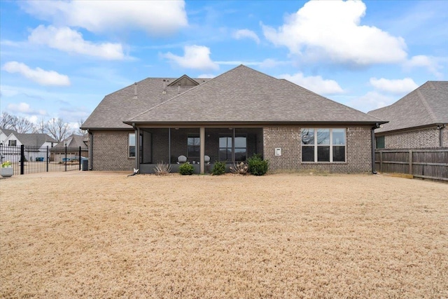 back of property featuring brick siding, a shingled roof, and a fenced backyard