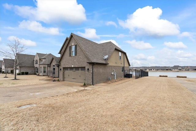 view of side of home with driveway, a water view, an attached garage, fence, and brick siding