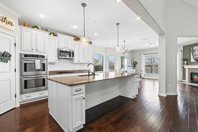 kitchen with stainless steel appliances, dark wood-type flooring, a sink, dark stone counters, and tasteful backsplash