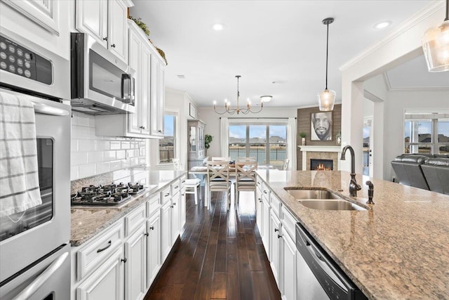 kitchen with a warm lit fireplace, a sink, ornamental molding, appliances with stainless steel finishes, and dark wood-style floors