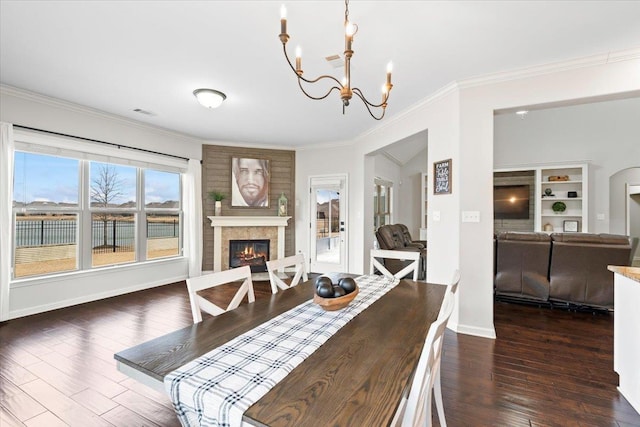 dining area featuring baseboards, a glass covered fireplace, wood finished floors, crown molding, and a notable chandelier