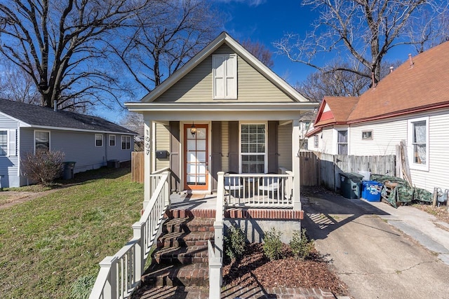 shotgun-style home with covered porch, fence, central AC, and a front yard