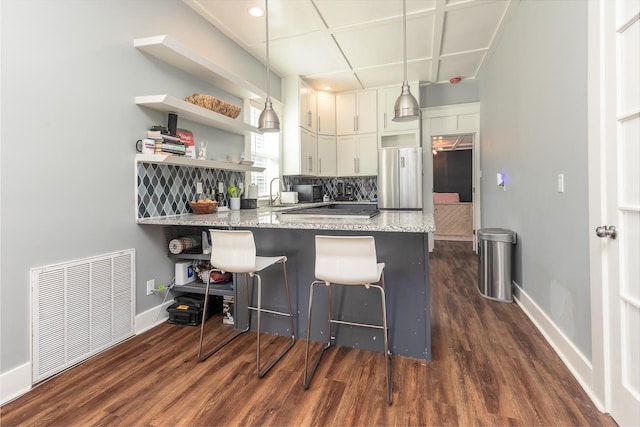 kitchen featuring open shelves, visible vents, decorative backsplash, freestanding refrigerator, and a peninsula