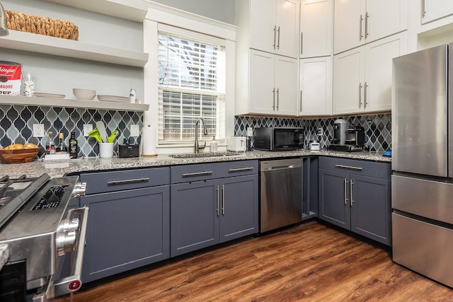 kitchen with appliances with stainless steel finishes, light stone countertops, a sink, and dark wood-style floors