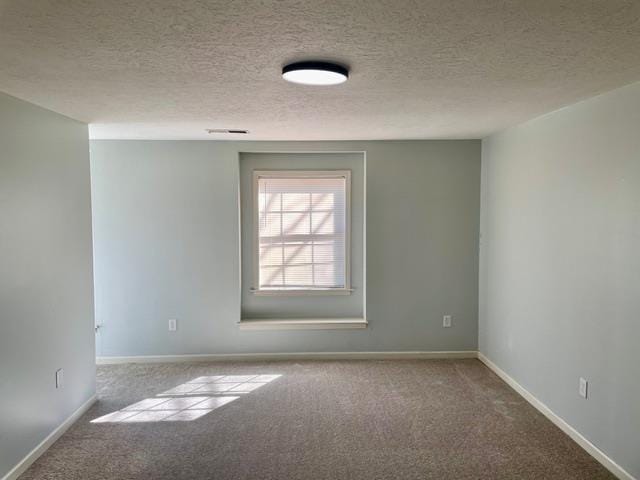 carpeted spare room featuring a textured ceiling, visible vents, and baseboards