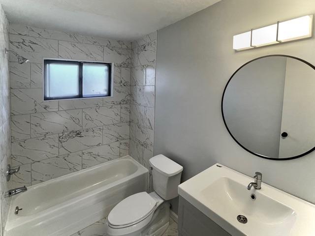 full bath with marble finish floor, tub / shower combination, vanity, and toilet