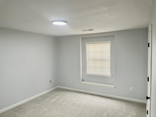 empty room featuring light carpet, visible vents, and baseboards